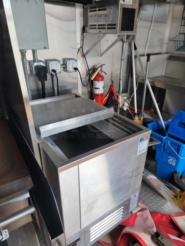 Stainless steel commercial ice bin in a food truck kitchen, sliding lid, vented panel, power outlets nearby, good condition.