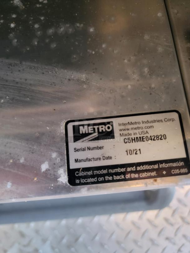 Metal cabinet with visible Metro label. Serial: C5HME042820, Manufacture Date: 10/21. Made in USA. Labels suggest location of model info. Scratched surface.
