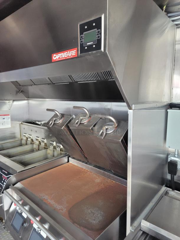 CaptiveAire commercial kitchen exhaust hood with control panel, above stainless steel fryers and griddle, appears in used condition.