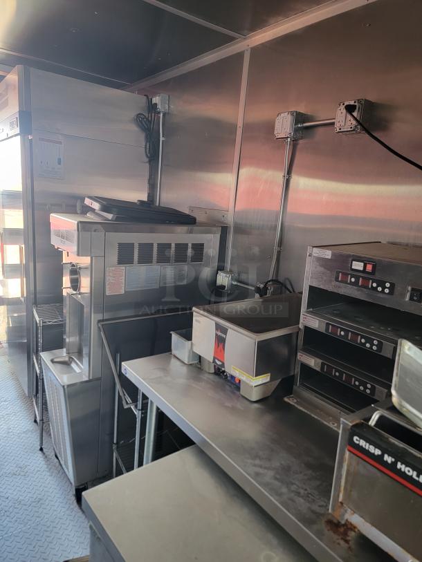 Commercial kitchen equipment featuring a countertop warmer, ovens, and stainless steel surfaces in used condition. Multiple electrical outlets are visible on the wall.