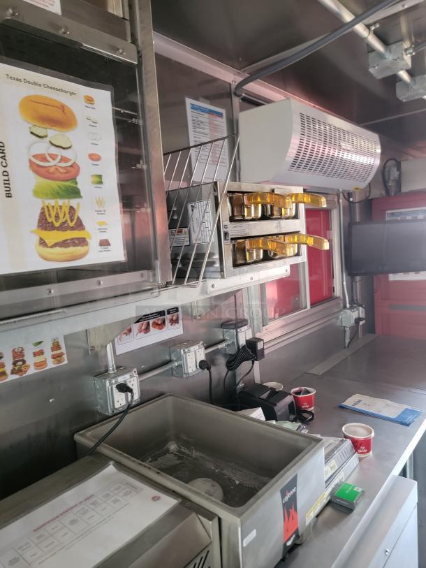 Food truck interior featuring stainless steel counters, a Texas Double Cheeseburger build card, and various cooking equipment.