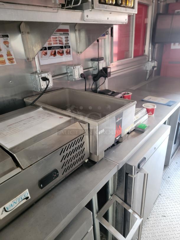 Stainless steel commercial kitchen setup with Avantco refrigeration unit, heating equipment, and food preparation space.