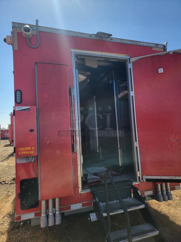 Red mobile unit with open door, showing interior. Visible markings: "120/208 V 3 PHASE." Equipped with security cameras.