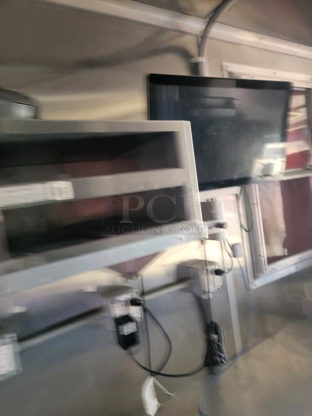 Interior view showing mounted flat-screen monitor and shelf with electrical outlets and cables, in good condition.
