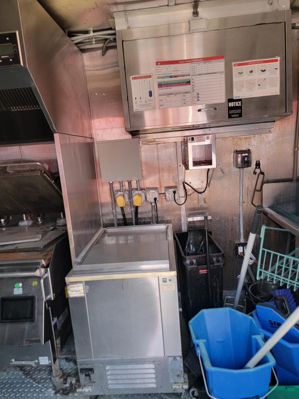 Commercial kitchen setup with stainless steel appliances, including a freezer and stovetop. Visible operation plan and cleaning tools.