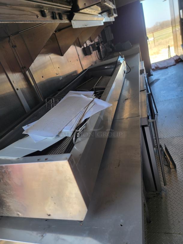 Commercial kitchen equipment with stainless steel countertop and ventilation hood, includes paper stacks and baskets, appears gently used.