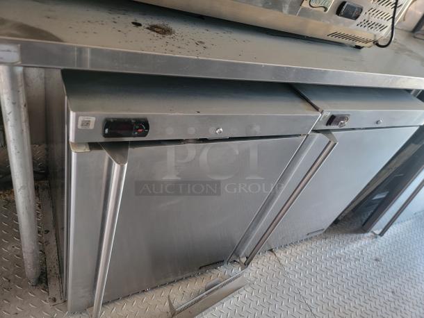 Stainless steel commercial refrigerator, double door, digital displays, visible wear, ideal for kitchen use.