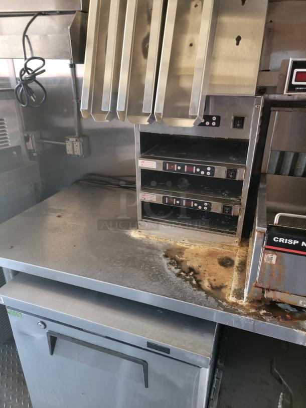 Commercial stainless steel kitchen workstation with food warmers, undercounter fridge, and signs of wear and residue.