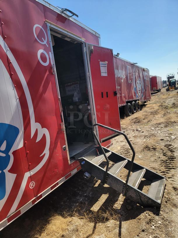 Red mobile kitchen trailer with Wendy's branding, exterior steps, open side door, logos, and visible dirt path.