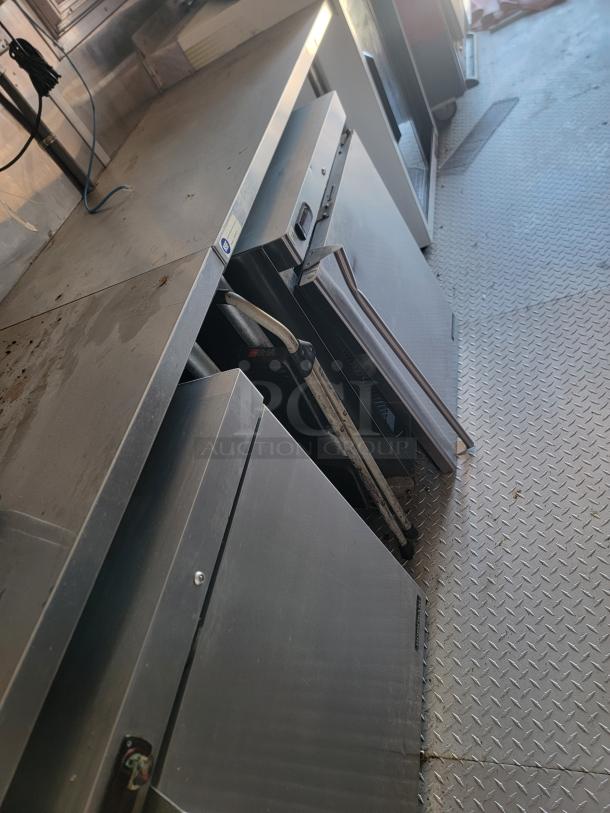 Commercial kitchen equipment, stainless steel work surfaces, appliances below, signs of wear. Ideal for professional kitchen use.