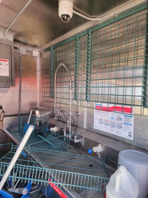 Stainless steel commercial sink area with sprayer faucet, storage racks, and Ecolab sanitizer instructions, in used condition.