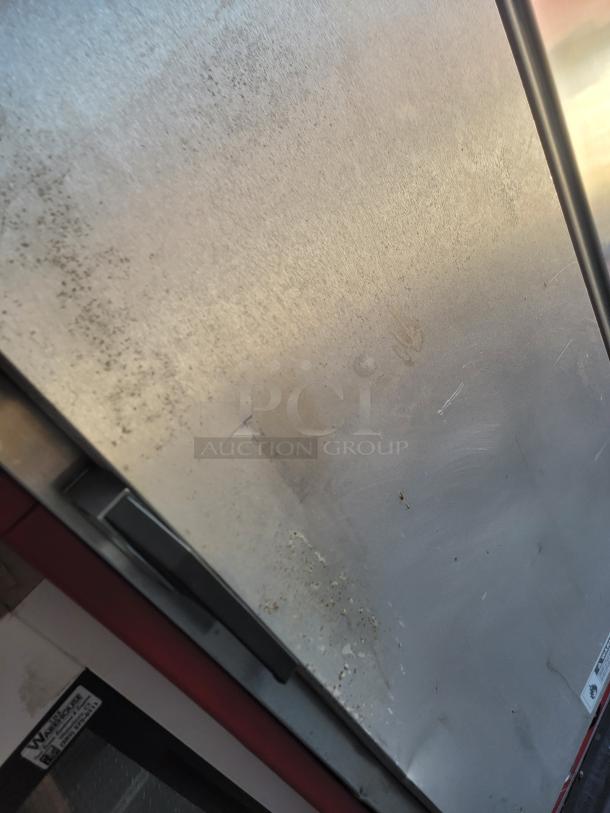 Industrial stainless steel door with weathered surface, showing signs of age and use. Small warning label visible at bottom.