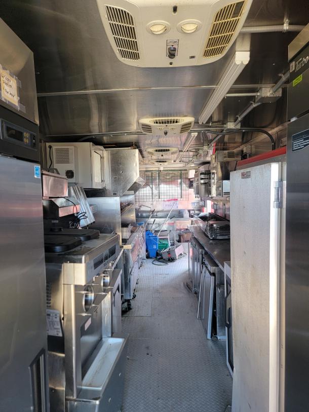 Interior view of a food truck kitchen with stainless steel appliances, including an oven, refrigerator, and grill in good condition.