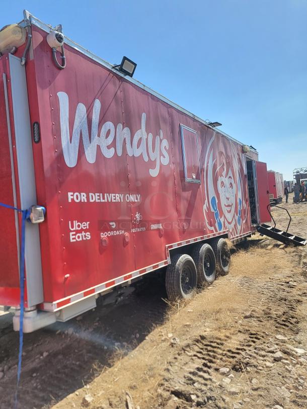 Red Wendy's food truck with delivery service logos, featuring triple axles and branding for Uber Eats, DoorDash, Postmates, and Grubhub.