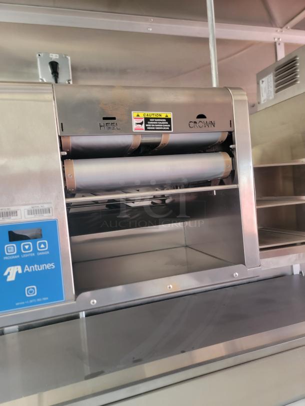 Antunes stainless steel toaster with caution label and visible rollers. Features "HEEL" and "CROWN" markings.