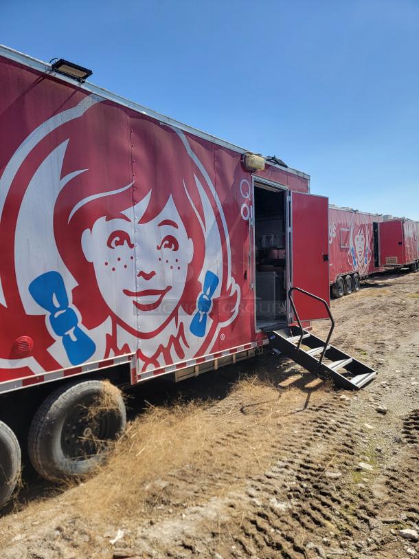 Red mobile trailer with a large graphic of a girl's face with red hair and blue bows, open door with stairs, moderate wear.