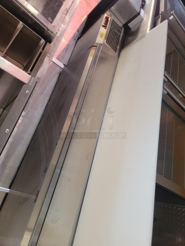 Stainless steel commercial refrigerator with white cutting board, control panel, and ventilation features visible, in mint condition.