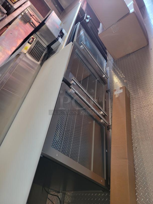 Stainless steel commercial refrigerator with glass doors, in excellent condition, surrounded by boxes.