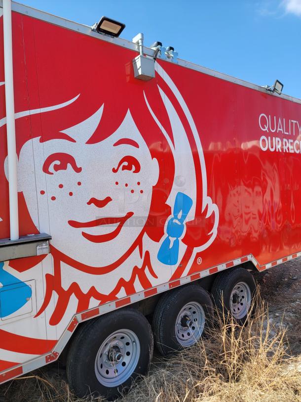Red mobile food trailer featuring a large Wendy's logo, equipped with floodlights and triple axle wheels. In good condition.