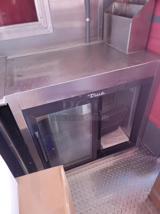 Stainless steel True under-counter refrigerator with double glass doors, visible logo, and sturdy metal construction.