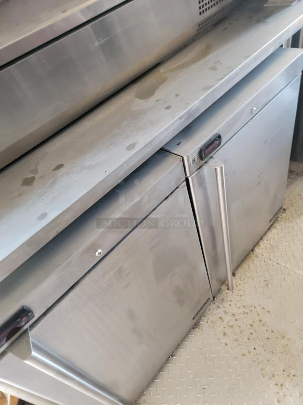 Stainless steel commercial refrigerator with dual doors, showing signs of wear and surface stains, used condition.