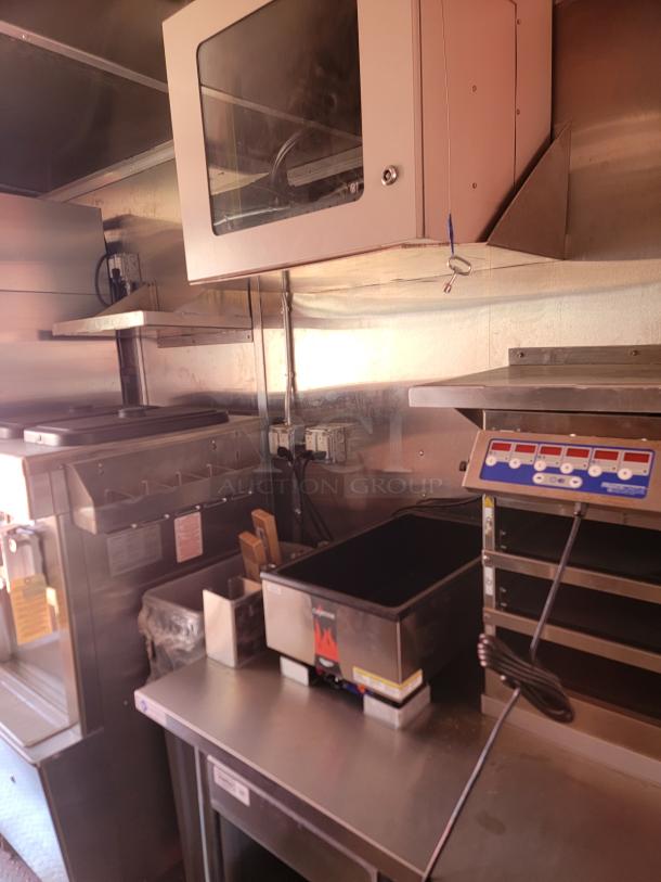 Commercial kitchen setup with stainless steel appliances, including a deep fryer, shelf storage, and a food warmer. Good condition.