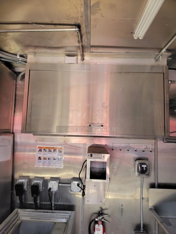 Stainless steel commercial kitchen cabinet with storage space. Features include electrical sockets and a fire extinguisher below.
