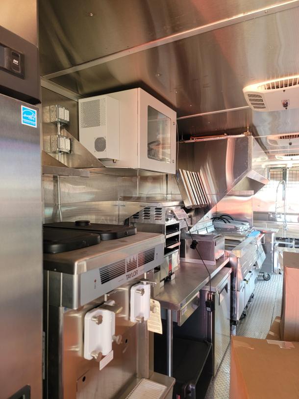 Commercial kitchen interior with Taylor soft-serve machine, stainless steel appliances, ventilation hood, and refrigeration unit.