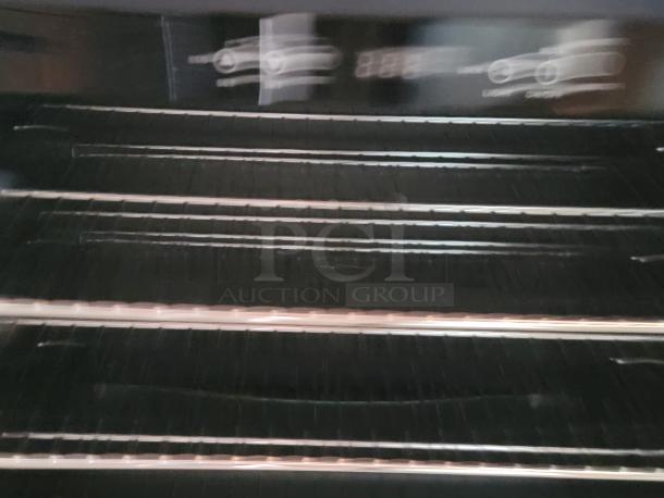 Blurry image of a stainless steel oven interior with multiple racks and faint control symbols.