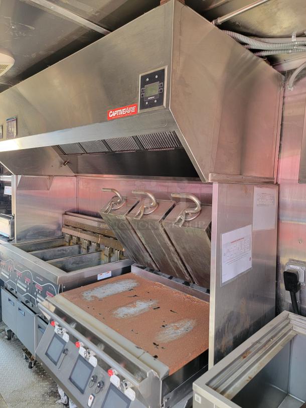 Commercial kitchen setup with CaptiveAire hood, multiple grills, and fryers. Features rust and wear. Hood has a control panel.