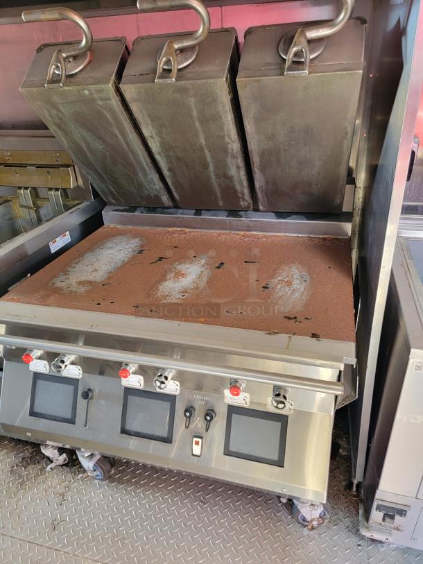 Commercial kitchen grill with three metal clamshell lids, control panel with knobs and buttons, on a patterned metal floor.