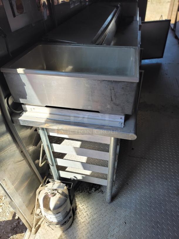 Industrial stainless steel sink with multiple compartments, mounted on a metal stand. Appears in fair condition.