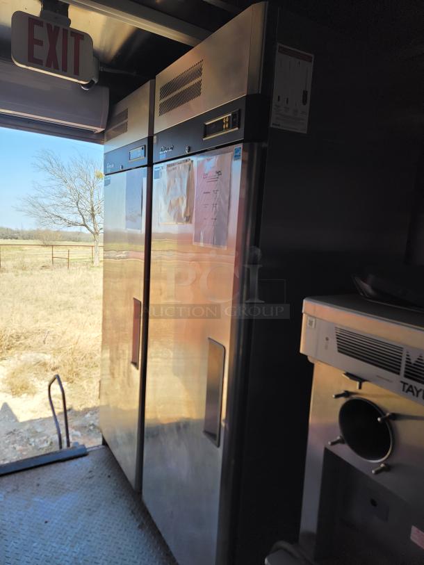 Commercial stainless steel refrigerator, double-door, with digital temperature displays and exterior documents. Visible “EXIT” sign above.
