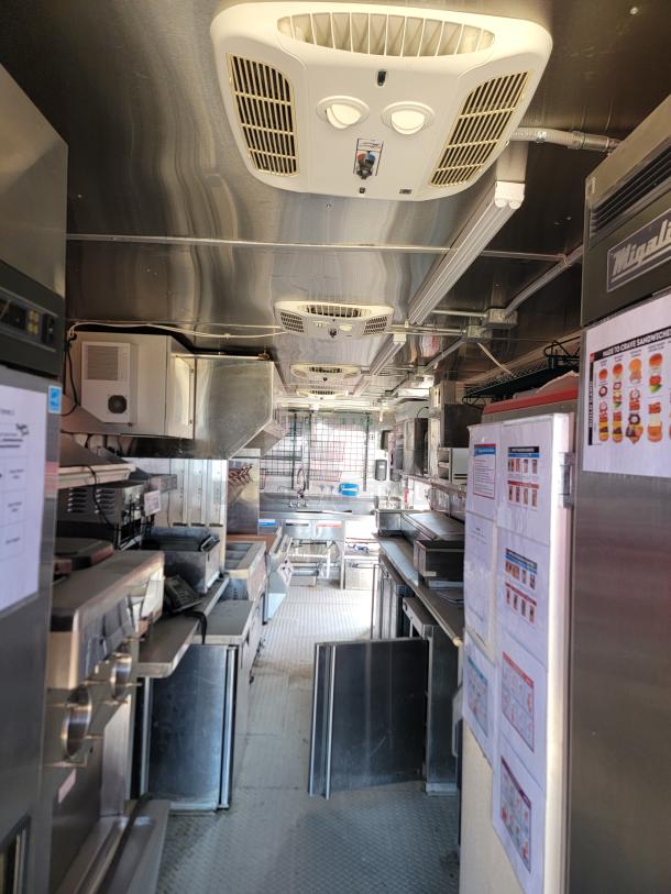 Interior of a mobile kitchen food truck with stainless steel appliances, air conditioning units, prep tables, and visible instruction sheets.