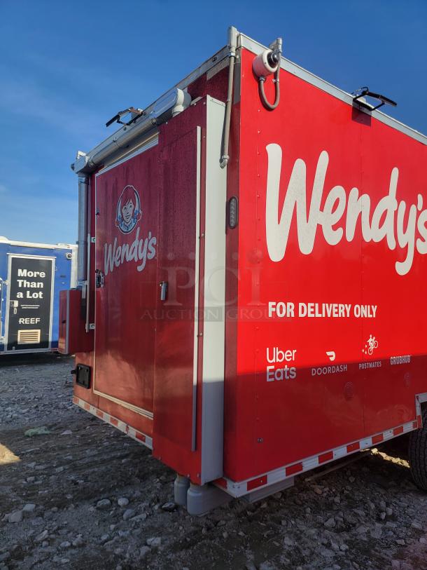 Red Wendy's delivery trailer with logos for Uber Eats, DoorDash, Postmates, and Grubhub; side view on a gravel lot.