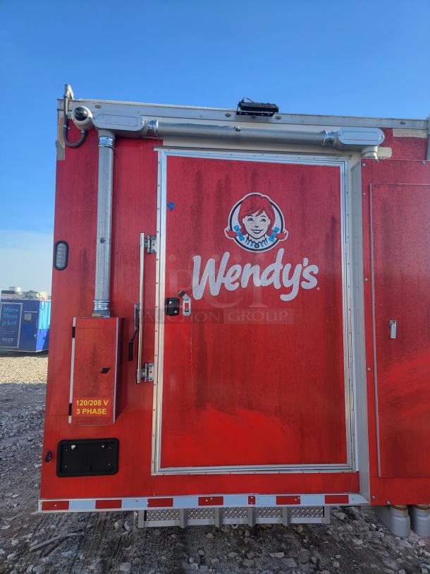 Red Wendy's mobile kitchen unit with logo, showing utility attachment and a "120/208 V 3 Phase" label on the door.