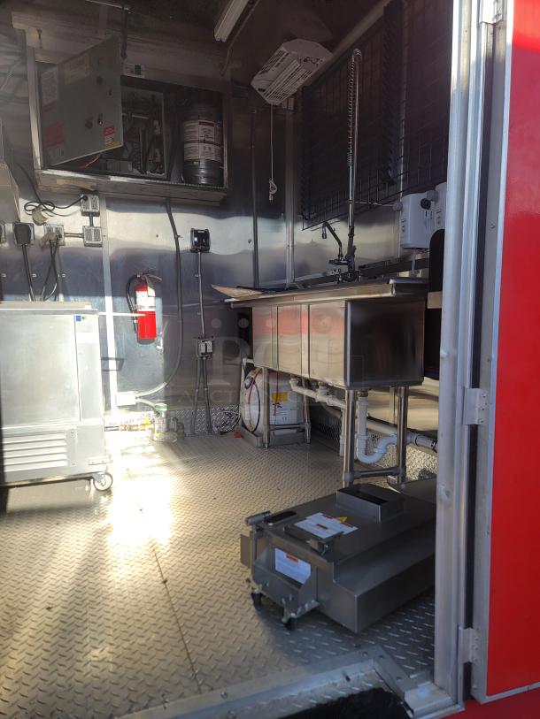 Commercial kitchen interior with stainless steel sink, fire extinguisher, and steel flooring. Includes open utility panel and storage.