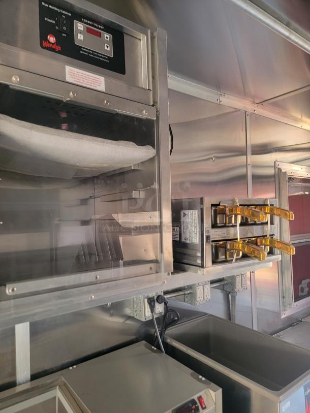 Stainless steel commercial kitchen with a Henry Penny bun heating cabinet, Wendy's branding, and dual toaster unit.
