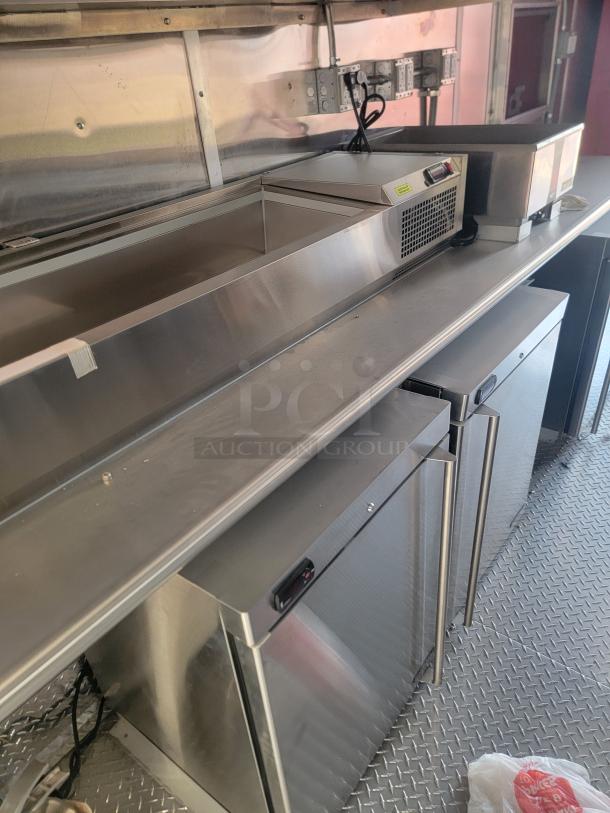 Stainless steel commercial kitchen equipment with dual refrigeration units, prep counter, and visible electrical outlets. Excellent condition.