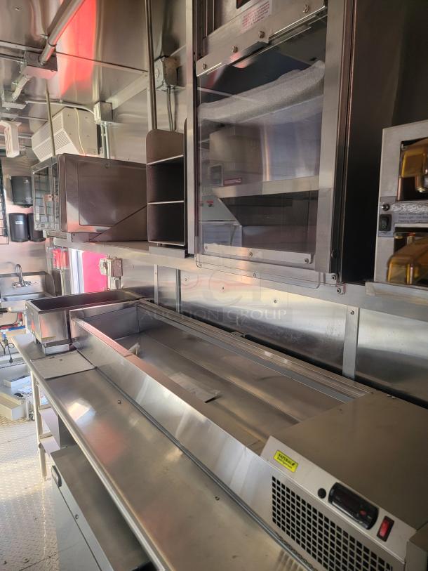 Industrial stainless steel kitchen setup featuring microwave, storage shelves, and refrigeration unit. Clean, modern condition.