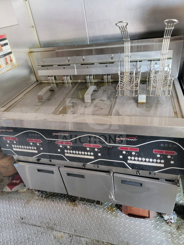 Henny Penny fryer setup in mobile kitchen trailer. Includes dual fryer compartments with digital controls, baskets, and CaptiveAire hood.