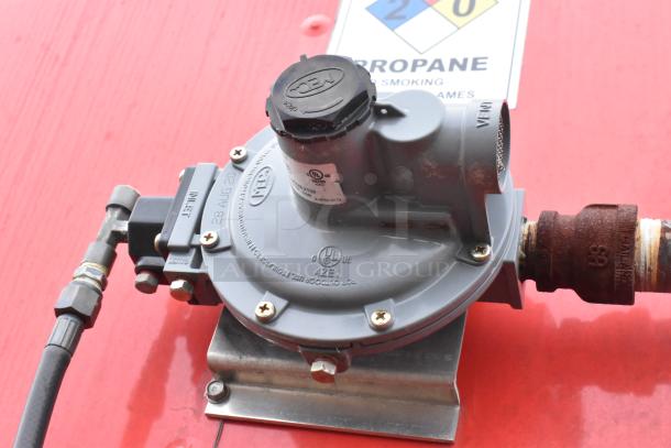 Propane regulator mounted on a red surface, labeled UL listed, with "28 AUG 20" marking. Nearby propane safety sign visible.