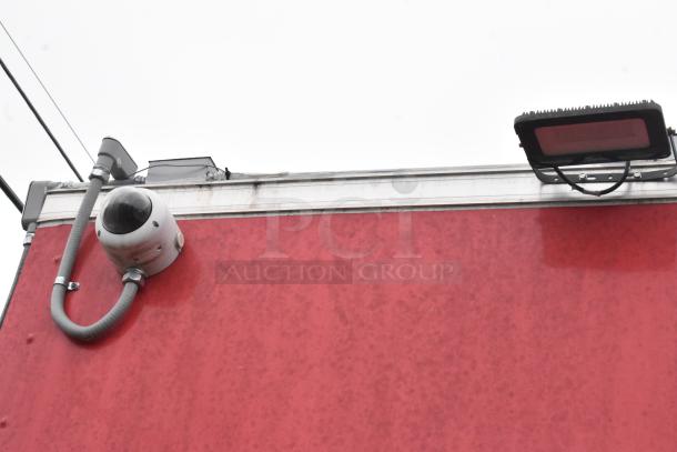 Red mobile kitchen trailer exterior, featuring surveillance camera and light fixture on top edge.