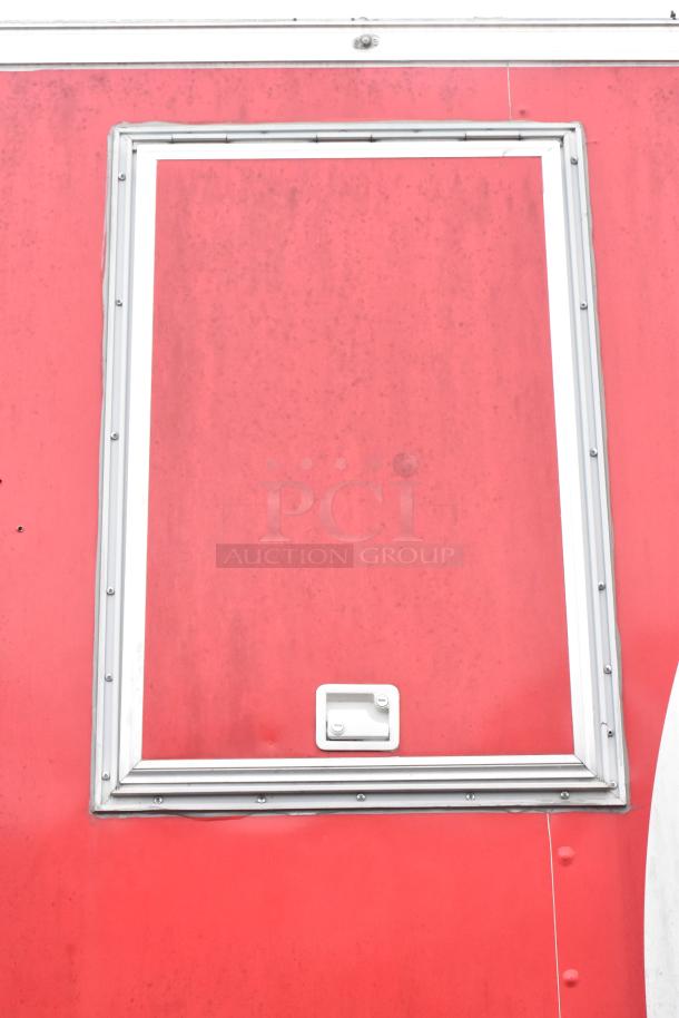 Red exterior of a brand new Wendy's mobile kitchen trailer with a window framed by metal trim.