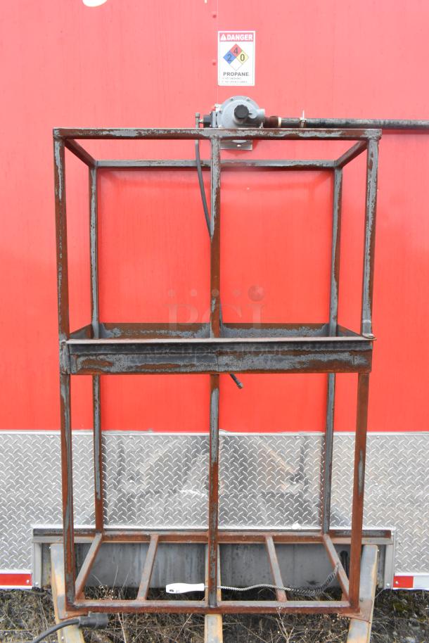 Rusty metal frame in front of red mobile kitchen trailer, featuring a propane warning sign above.