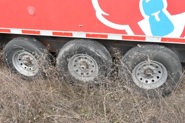 Triple axle of 8.5' x 28' Wendy's mobile kitchen trailer in excellent condition. Red exterior with visible wheel section.