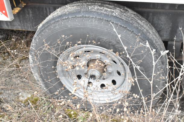 Close-up image of a tire on a Wendy's mobile kitchen trailer surrounded by dry grass.