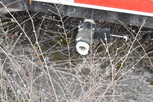 Close-up of a valve under a Wendy's mobile kitchen trailer, surrounded by dry foliage. Valve part of plumbing system.