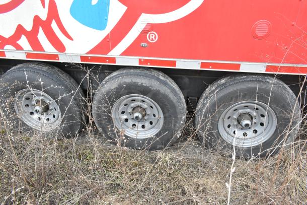 Triple axle wheels of a new 8.5' x 28' Wendy's mobile kitchen trailer with red exterior design.