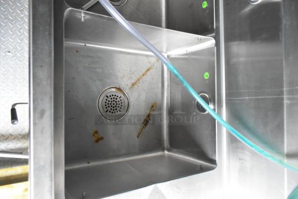 Interior view of Wendy's mobile kitchen trailer sink, stainless steel, showing drainage and plumbing setup.